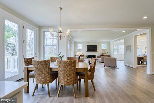 dining room featuring hardwood / wood-style floors, a large fireplace, a healthy amount of sunlight, and a notable chandelier