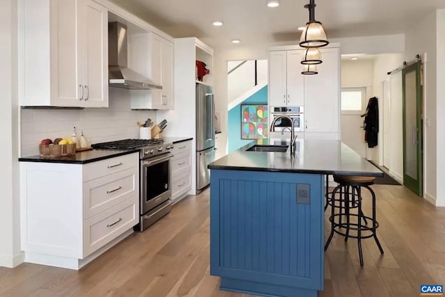 kitchen featuring wall chimney range hood, sink, a barn door, white cabinetry, and stainless steel appliances