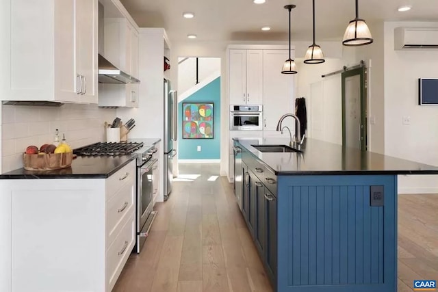 kitchen with sink, hanging light fixtures, a barn door, appliances with stainless steel finishes, and white cabinetry