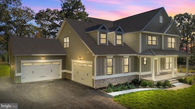 view of front of house with covered porch, an attached garage, board and batten siding, stone siding, and driveway