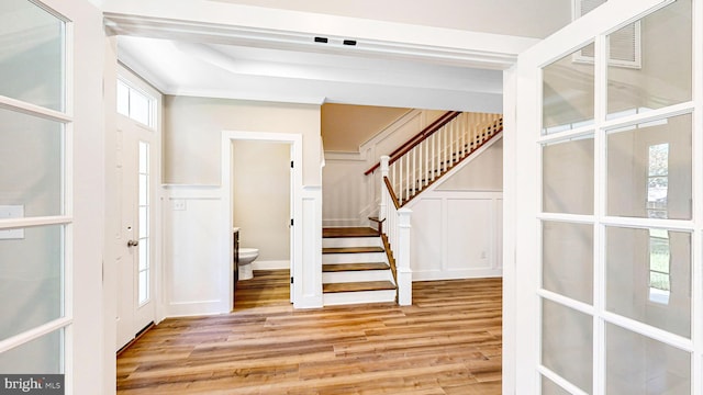 entrance foyer featuring light wood-type flooring, stairway, a decorative wall, and wainscoting