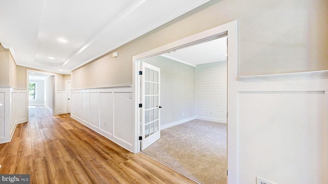 corridor featuring light wood-style flooring, a decorative wall, crown molding, and wainscoting