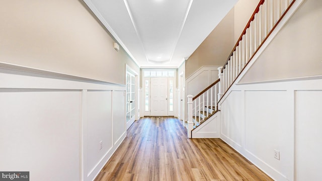 entryway featuring wainscoting, a decorative wall, light wood-style flooring, and stairs