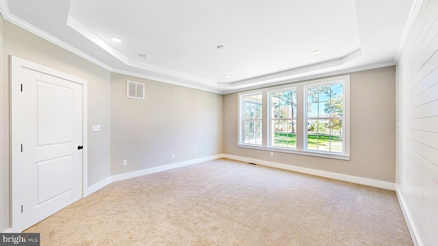 empty room featuring light colored carpet, a raised ceiling, visible vents, and crown molding