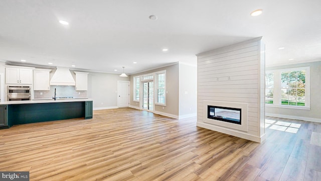 unfurnished living room featuring recessed lighting, a fireplace, light wood-style flooring, and crown molding