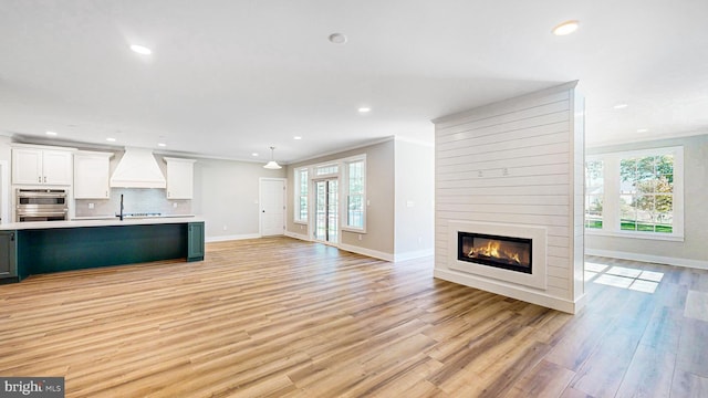 unfurnished living room featuring a large fireplace, recessed lighting, light wood-type flooring, and crown molding