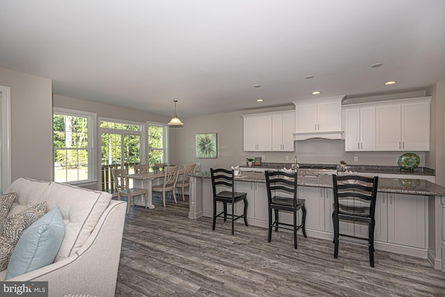 kitchen with a kitchen breakfast bar, dark stone countertops, pendant lighting, white cabinets, and dark hardwood / wood-style flooring