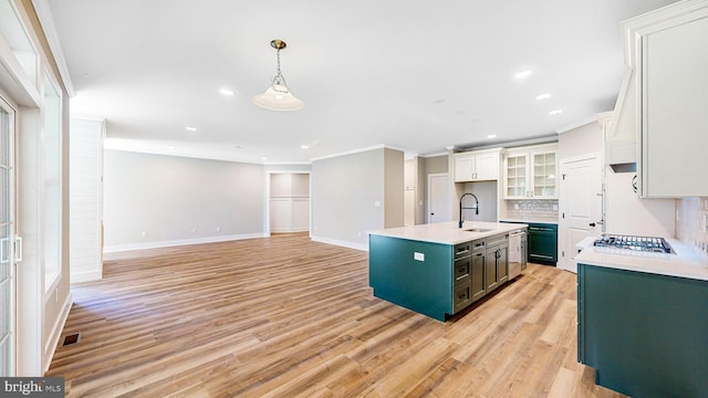 kitchen featuring a sink, white cabinets, light countertops, a center island with sink, and pendant lighting