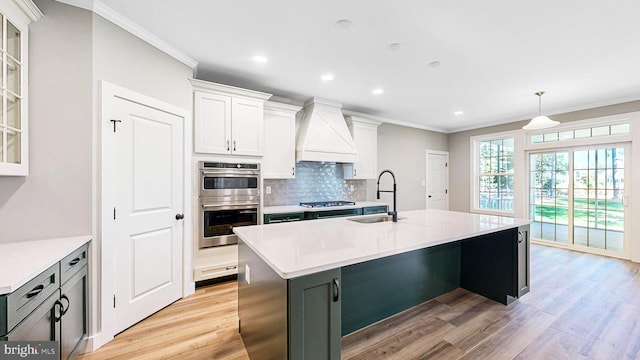 kitchen with a center island with sink, custom range hood, light countertops, white cabinetry, and a sink