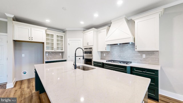 kitchen with custom range hood, glass insert cabinets, white cabinets, and a center island with sink