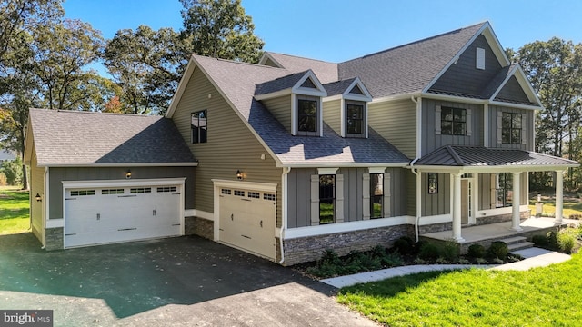 view of front facade featuring a garage, stone siding, roof with shingles, covered porch, and board and batten siding