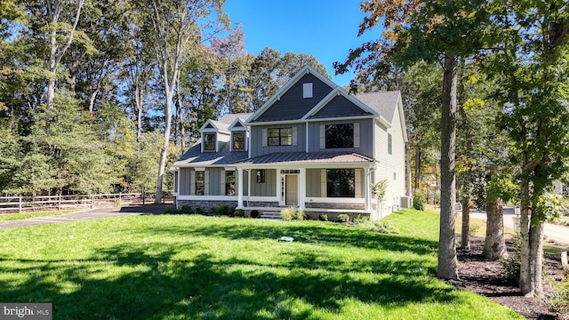 view of front of home with a standing seam roof, covered porch, fence, board and batten siding, and a front yard