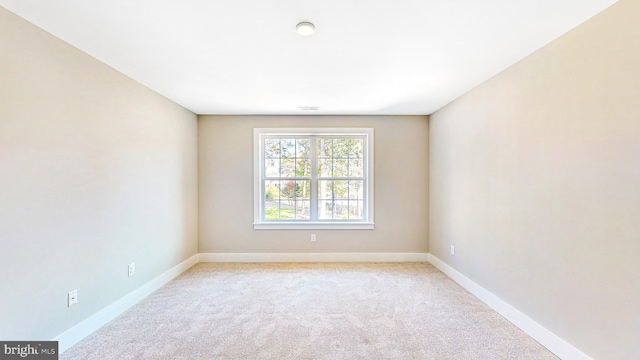 spare room featuring light carpet and baseboards