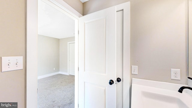 hallway featuring carpet floors, baseboards, and a sink