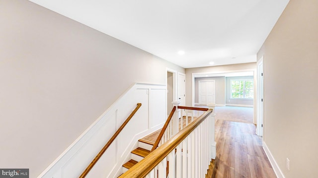 corridor with light wood-style floors, baseboards, and an upstairs landing