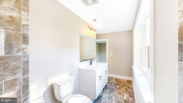 bathroom featuring visible vents, baseboards, toilet, stone finish floor, and vanity