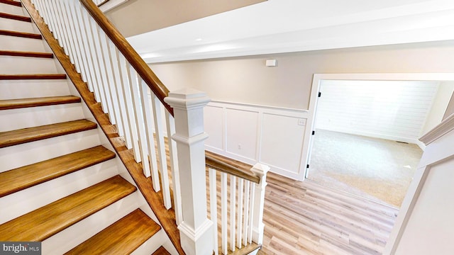 staircase with wainscoting, a decorative wall, and wood finished floors