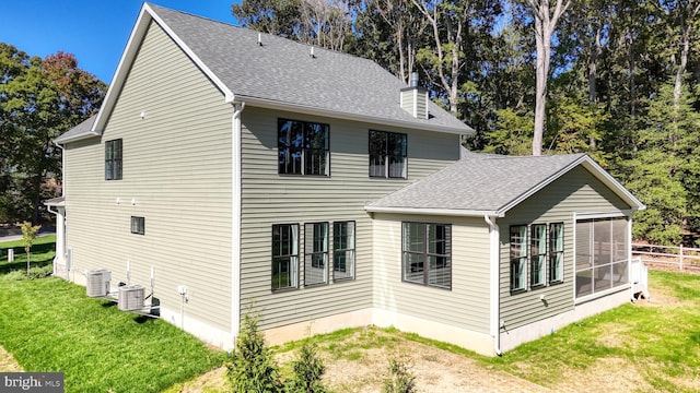 exterior space with a shingled roof, a sunroom, a chimney, cooling unit, and a yard