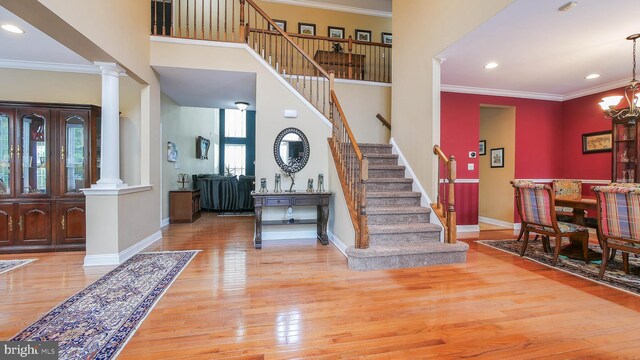 foyer entrance with a towering ceiling, light wood-type flooring, decorative columns, crown molding, and a notable chandelier