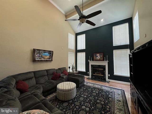 living room featuring hardwood / wood-style floors, high vaulted ceiling, crown molding, ceiling fan, and a premium fireplace