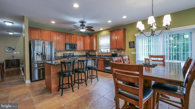 kitchen featuring pendant lighting, a center island, ceiling fan with notable chandelier, decorative backsplash, and appliances with stainless steel finishes