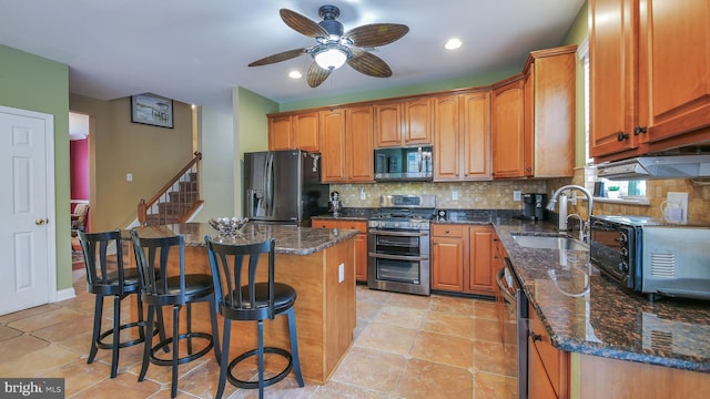 kitchen with sink, a breakfast bar area, ceiling fan, a kitchen island, and stainless steel appliances