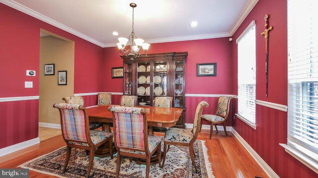 dining area with light wood-type flooring, an inviting chandelier, plenty of natural light, and ornamental molding