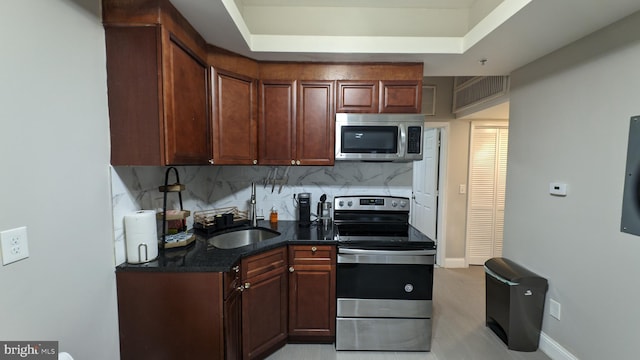 kitchen featuring tasteful backsplash, dark stone counters, stainless steel appliances, a tray ceiling, and sink