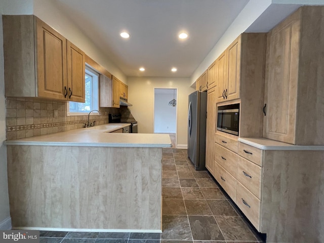 kitchen featuring sink, backsplash, kitchen peninsula, light brown cabinetry, and appliances with stainless steel finishes