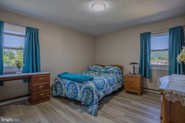 bedroom with light hardwood / wood-style floors, a textured ceiling, and a baseboard radiator