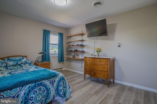 bedroom with a textured ceiling, light wood-type flooring, and baseboard heating