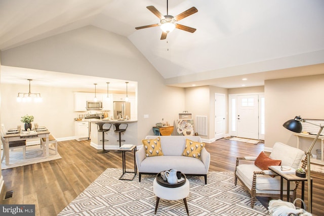 living room featuring ceiling fan with notable chandelier, light hardwood / wood-style flooring, and vaulted ceiling