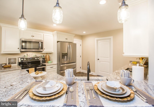 kitchen with light stone countertops, white cabinets, pendant lighting, and appliances with stainless steel finishes