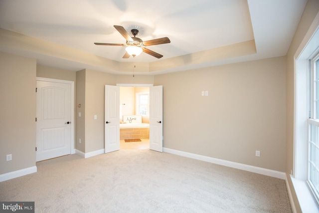 unfurnished bedroom with ceiling fan, light carpet, a tray ceiling, and ensuite bathroom