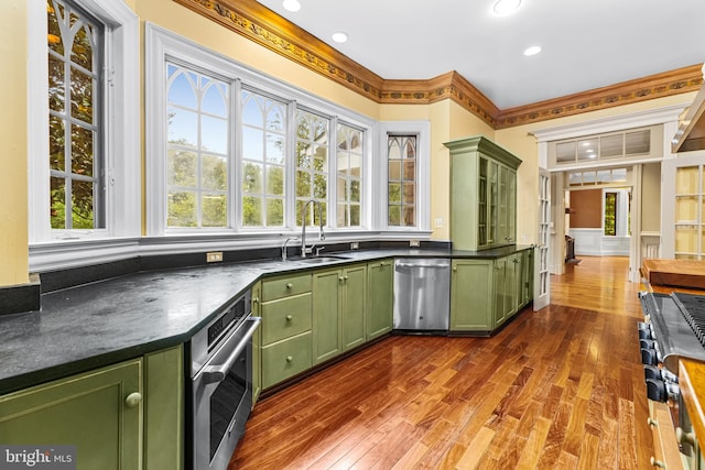 kitchen with dark wood-type flooring, green cabinets, sink, ornamental molding, and stainless steel appliances