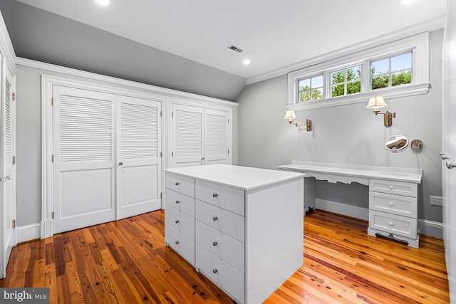 home office featuring lofted ceiling, built in desk, light wood-type flooring, and ornamental molding