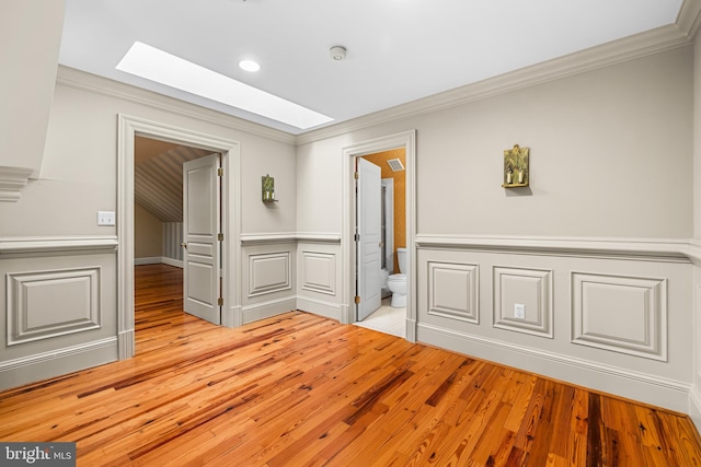 interior space with a skylight, ornamental molding, and light hardwood / wood-style floors