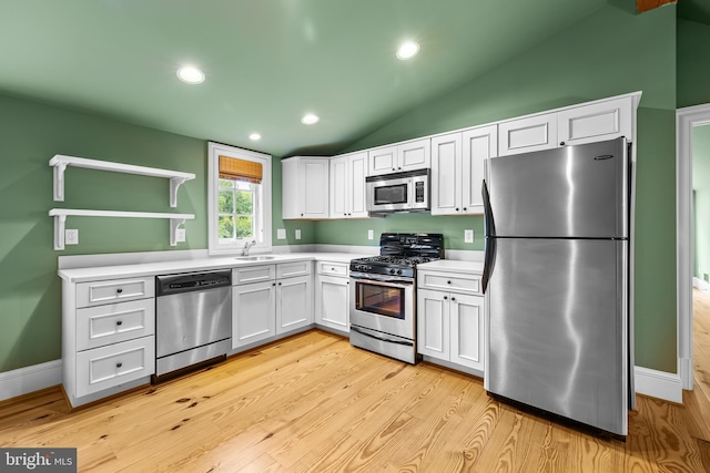 kitchen with white cabinets, sink, vaulted ceiling, light wood-type flooring, and appliances with stainless steel finishes