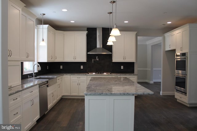 kitchen featuring wall chimney exhaust hood, decorative light fixtures, a kitchen island, light stone counters, and white cabinetry