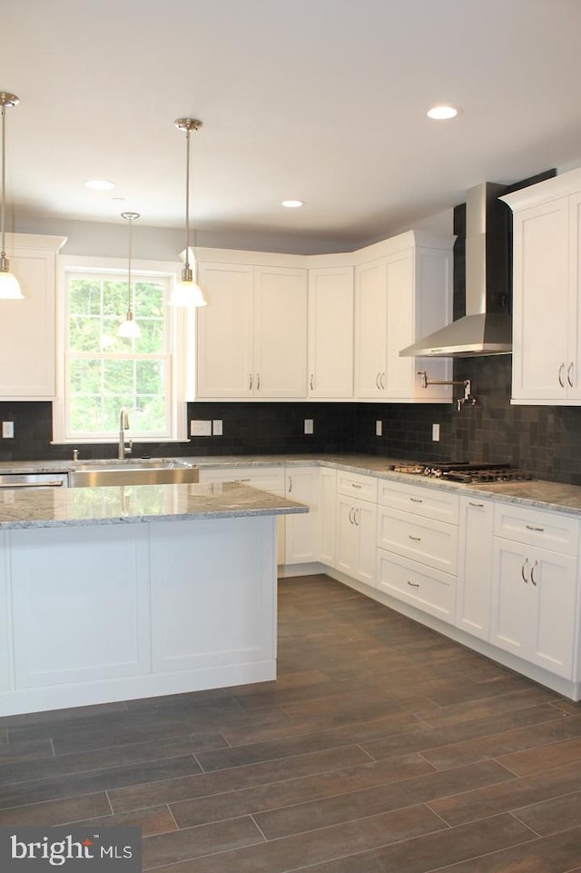 kitchen featuring light stone countertops, wall chimney exhaust hood, sink, decorative light fixtures, and white cabinetry