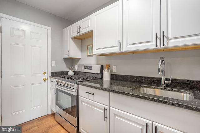 kitchen with sink, white cabinets, stainless steel gas range, and dark stone countertops