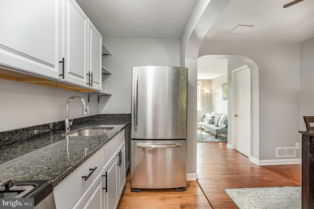 kitchen featuring sink, white cabinets, light hardwood / wood-style flooring, dark stone counters, and stainless steel fridge