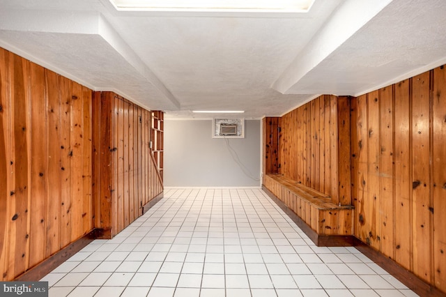 interior space featuring wood walls, a textured ceiling, light tile patterned floors, and an AC wall unit