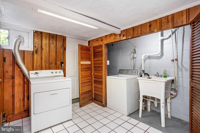 clothes washing area featuring light tile patterned flooring, sink, independent washer and dryer, and wooden walls