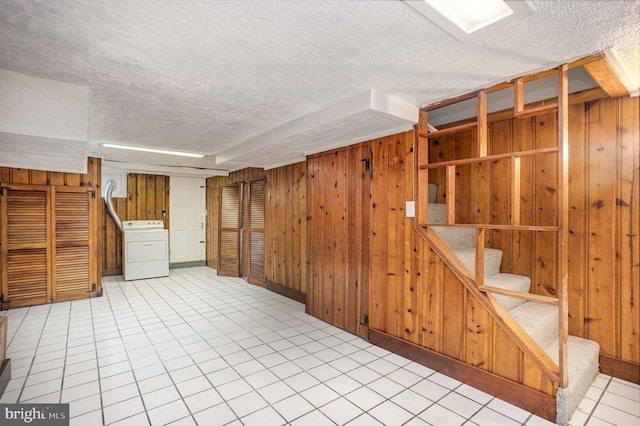 basement featuring light tile patterned floors, wooden walls, washer / clothes dryer, and a textured ceiling