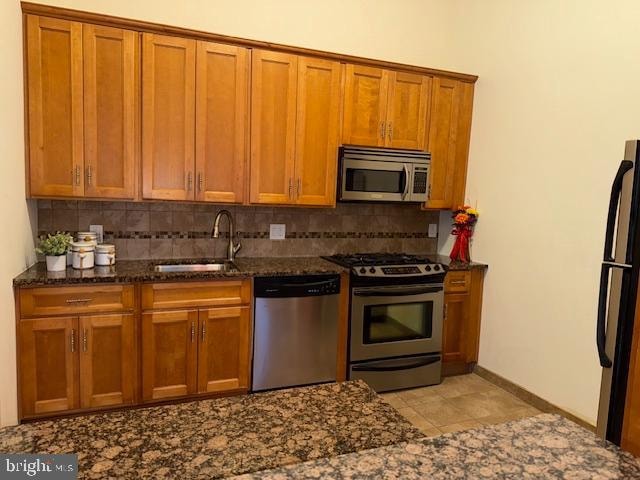 kitchen featuring dark stone countertops, stainless steel appliances, decorative backsplash, and sink