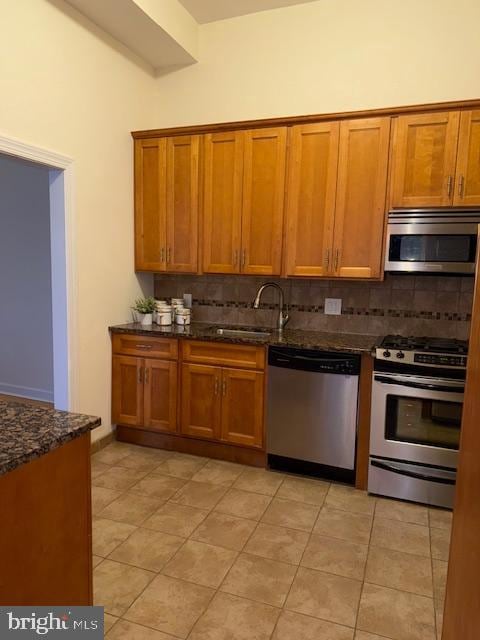 kitchen with appliances with stainless steel finishes, sink, dark stone counters, decorative backsplash, and light tile patterned floors