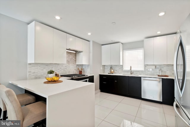 kitchen featuring backsplash, stainless steel appliances, light tile patterned floors, kitchen peninsula, and a breakfast bar