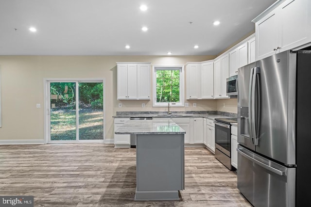 kitchen featuring a center island, white cabinets, light wood-type flooring, light stone countertops, and appliances with stainless steel finishes