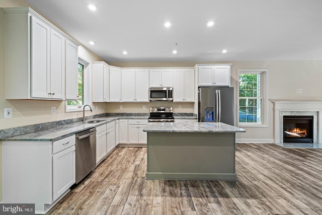 kitchen featuring appliances with stainless steel finishes, light stone counters, a kitchen island, a fireplace, and white cabinetry